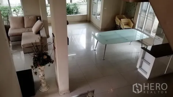 บ้าน ให้เช่าในLat Krabang, Bangkok - มุมมองจากบันไดลงสู่ชั้นล่าง เห็นโต๊ะทานอาหารกระจก โซฟา และหน้าต่างริมสวน