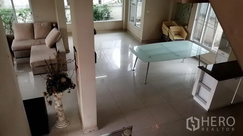 บ้าน ให้เช่าในLat Krabang, Bangkok - มุมมองจากบันไดลงสู่ชั้นล่าง เห็นโต๊ะทานอาหารกระจก โซฟา และหน้าต่างริมสวน