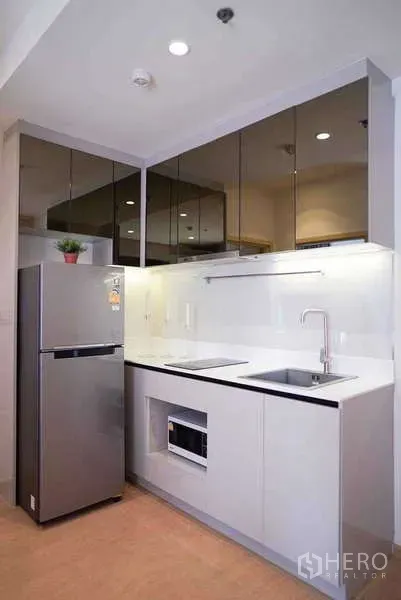 Condominium for rent or sale in Watthana, Bangkok - Modern kitchenette with glossy cabinets, stainless refrigerator, microwave niche, and sink under task lighting.