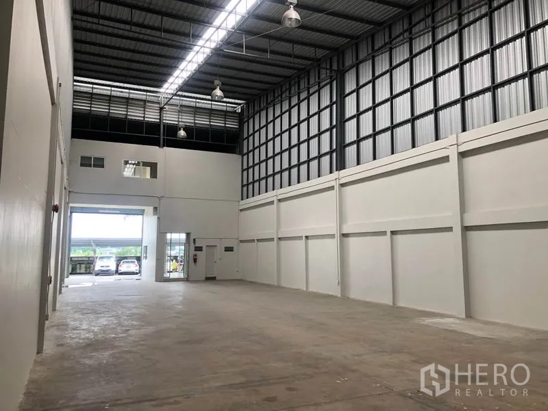 工厂 出租在Pak Kret, Nonthaburi - 仓库侧向视角，通风百叶与开启的卷闸门通向停车区。