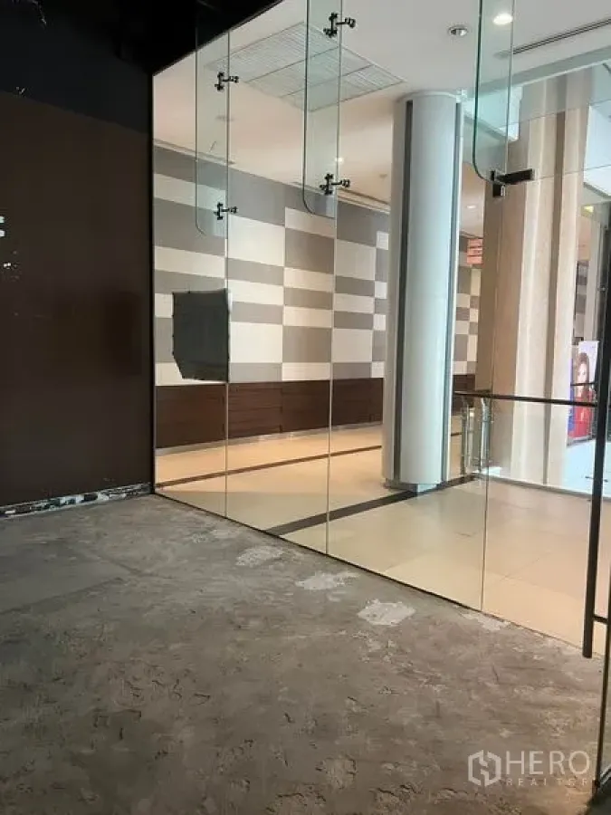 零售空间 出租在Watthana, Bangkok - 曼谷瓦他纳区购物走廊旁的小型商铺，落地玻璃门面与水泥地面，空间通透明亮。