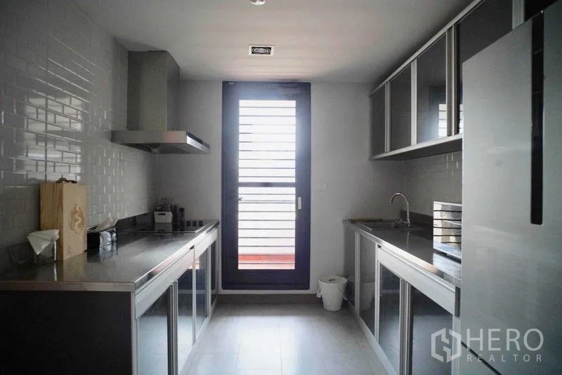 Condominium for rent in Watthana, Bangkok - Modern galley kitchen with stainless steel counters, range hood and glass-front cabinets.