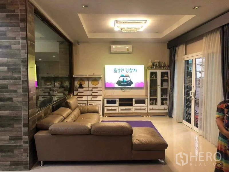 独立式住宅 出租或出售在Prawet, Bangkok - 客厅配皮质转角沙发、电视墙与推拉门