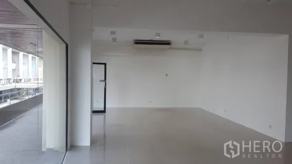 Office Space for rent in Khlong Toei, Bangkok - Spacious office interior featuring large windows, track lighting and a wall-mounted air-conditioner overlooking the building walkway.