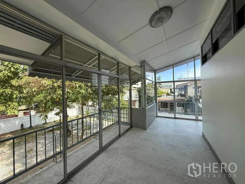 独立式住宅 出租在Watthana, Bangkok - 玻璃封闭式日光房与阳台，可俯瞰树木与社区景观。