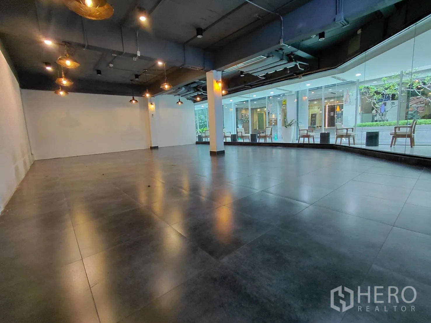 零售空间 for rent in Ratchathewi, Bangkok - 宽阔玻璃门面朝向室内中庭，可见座椅与绿化，深色地面开阔。