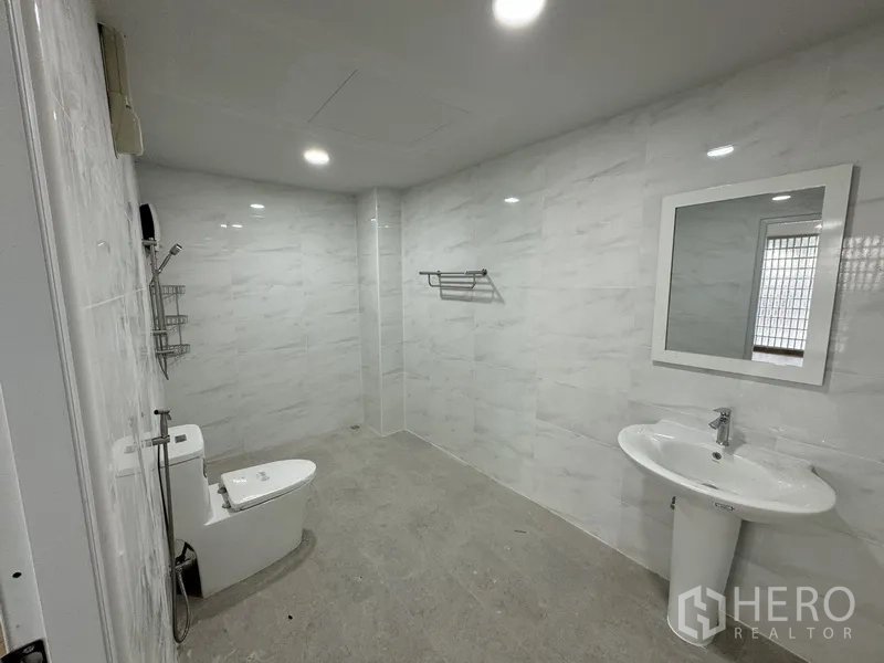 Townhouse for sale in Bueng Kum, Bangkok - Modern bathroom with white marble-style tiles, shower area, toilet and pedestal sink.