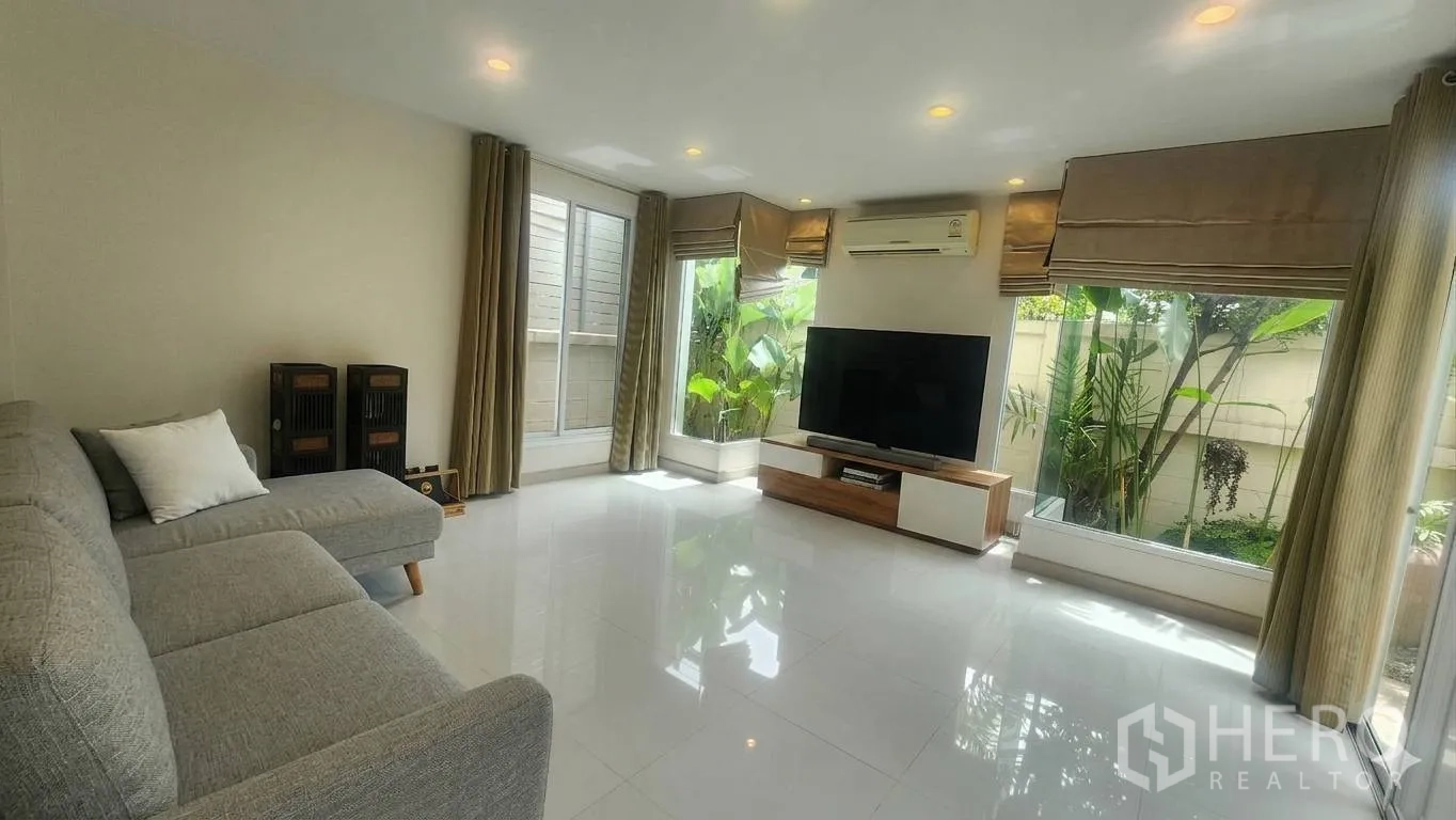 บ้านเดี่ยว for rent in Watthana, Bangkok - ห้องนั่งเล่นสว่าง ผนังกระจก โซฟาผ้า และชั้นวางทีวี