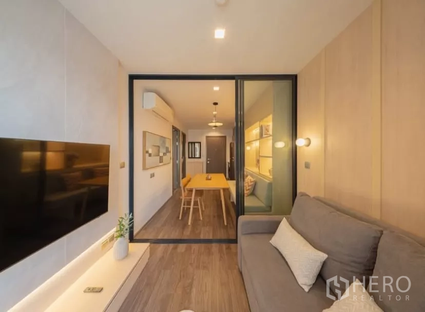 คอนโด ให้เช่าในChatuchak, Bangkok - ห้องนั่งเล่นสไตล์อบอุ่น โซฟาสีเทาและทีวีติดผนัง มองผ่านประตูกระจกบานเลื่อน