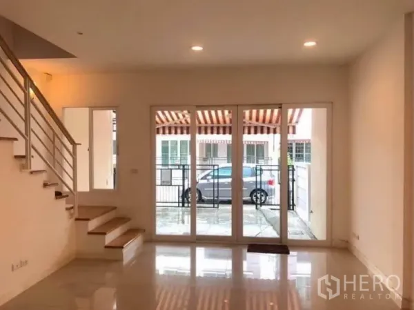 ทาวน์เฮาส์ ให้เช่าในWang Thonglang, Bangkok - ห้องนั่งเล่นเปิดโล่งมองออกสู่ลานหน้าบ้านและที่จอดรถผ่านประตูกระจกกว้าง เห็นรั้วเหล็กและกันสาด