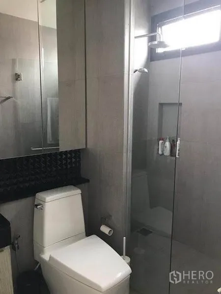 Townhouse for rent in Khlong Toei, Bangkok - Modern bathroom with toilet, glass shower enclosure and wall mirror.