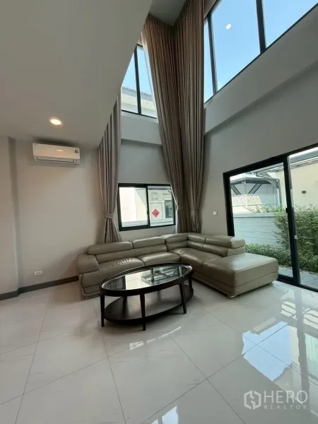 Townhouse for rent - Double‑height living room with floor‑to‑ceiling windows, L‑shaped leather sofa and a glass coffee table.