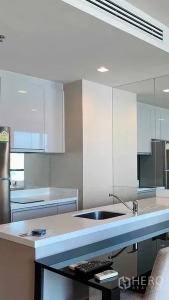 Condominium for rent or sale in Bang Rak, Bangkok - Bright modern kitchen with white cabinets, island sink, mirrored backsplash and stainless refrigerator in a Bangkok condo.