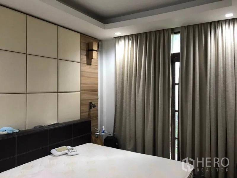 独立式住宅 出售在Lat Phrao, Bangkok - 主卧配软包床头墙与木饰面，托盘天花及全遮光窗帘。