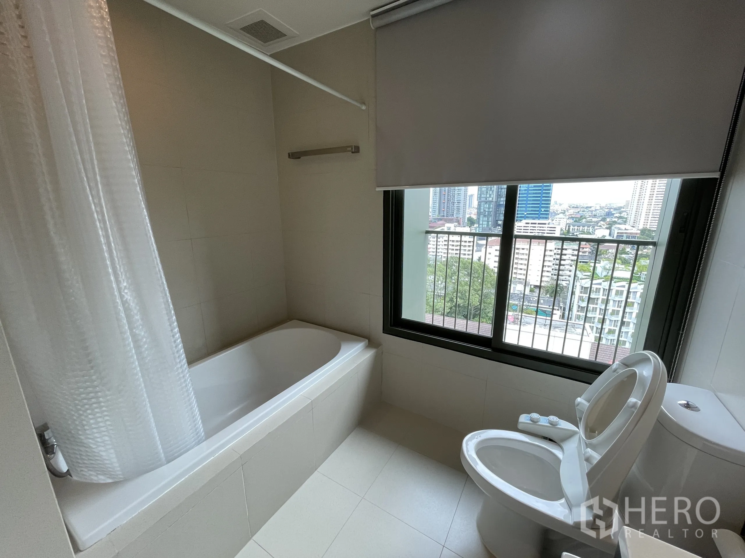 公寓 出租在Watthana, Bangkok - 浴室配浴缸与马桶，窗外可见城市景观。