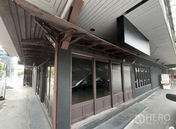 零售空间 出租在Watthana, Bangkok - 一层转角铺面，深色木檐与整面落地玻璃门窗。