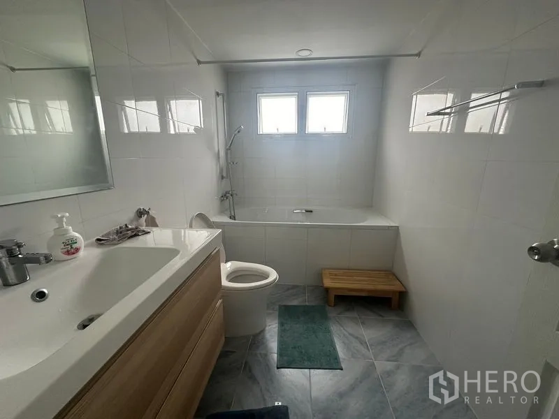 Condominium for rent - Clean bathroom with bathtub, vanity, toilet and a small wooden bench by the window.