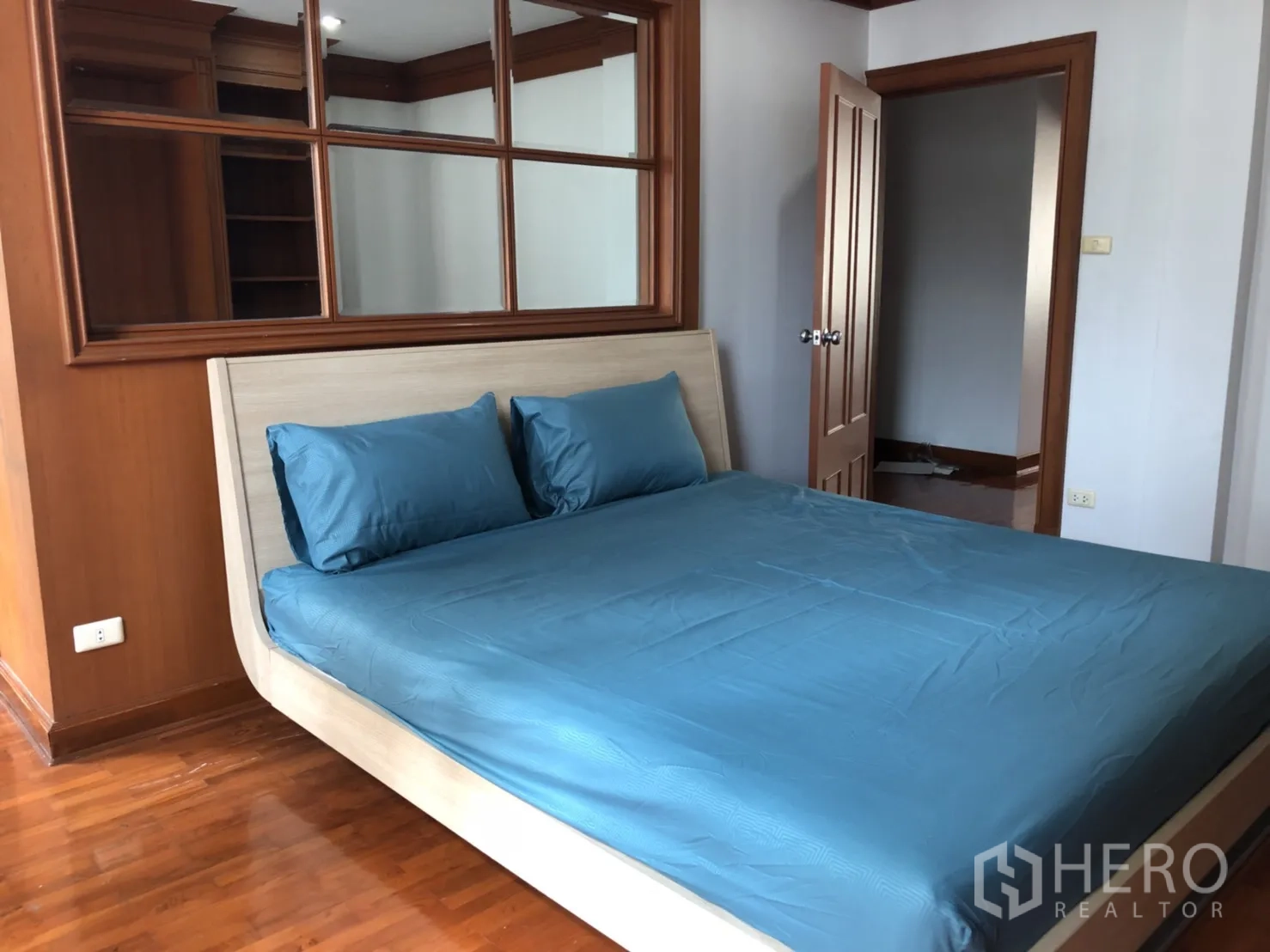 Townhouse for rent in Khlong Toei, Bangkok - Bedroom with blue bedding, mirror wall and wood trim.