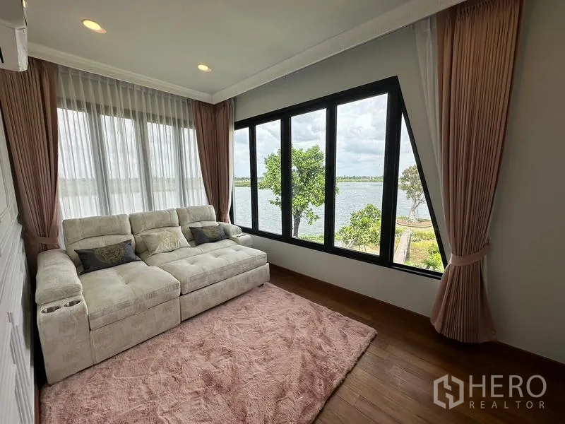Detached House for sale in Sai Noi, Nonthaburi - Lake-view family room with large corner windows, plush sofa and curtains.