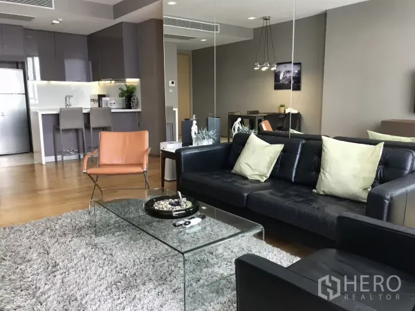 Condominium for rent in Watthana, Bangkok - Bright open-plan living room with black leather sofa, glass coffee table, and kitchen bar.