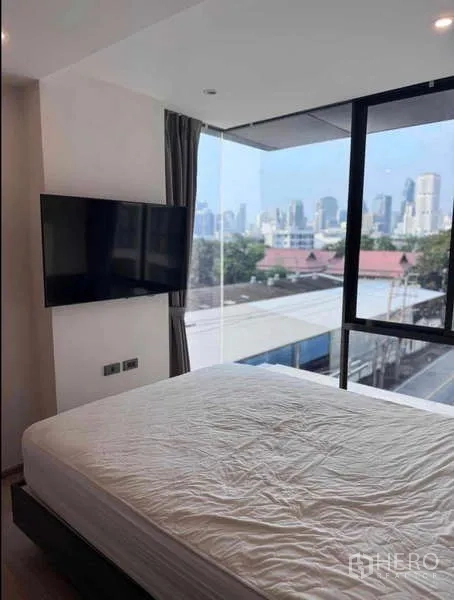Condominium for rent in Khlong Toei, Bangkok - Corner bedroom with city skyline view and wall-mounted TV.