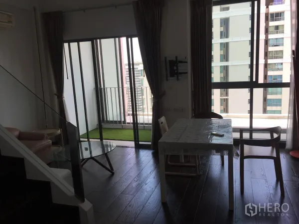 Condominium for rent in Ratchathewi, Bangkok - Living and dining space opening to a balcony with artificial grass and city view near Phaya Thai BTS.