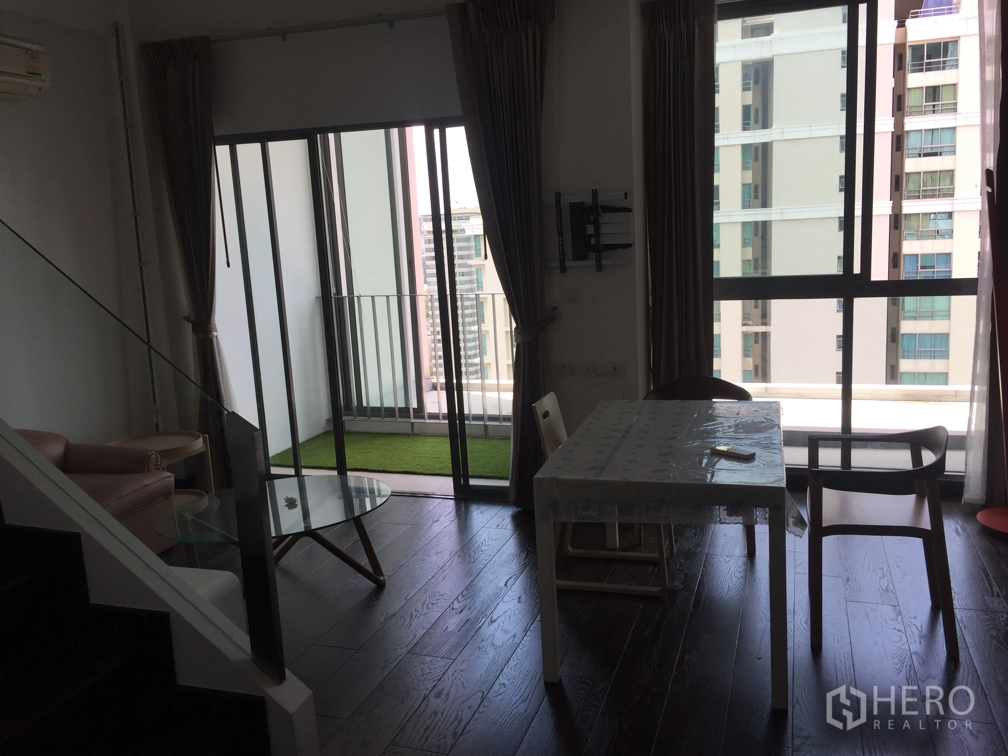 Condominium for rent in Ratchathewi, Bangkok - Living and dining space opening to a balcony with artificial grass and city view near Phaya Thai BTS.