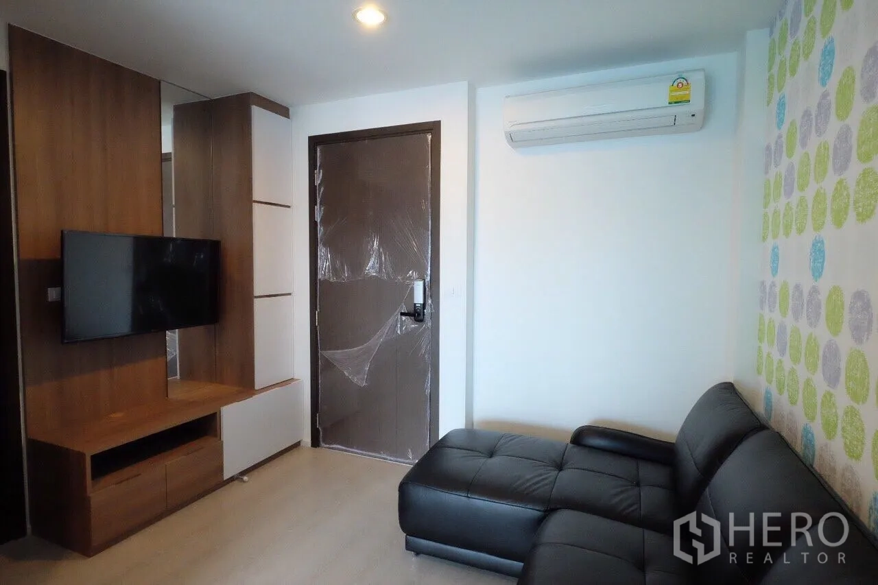 公寓 出租在Sathon, Bangkok - 客厅电视墙与入户门，配黑色沙发和空调，沙吞区公寓。