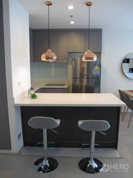 คอนโด ให้เช่าหรือขายในKhlong Toei, Bangkok - ครัวโทนเทาเคาน์เตอร์บาร์สีขาวพร้อมสตูลสองตัวและโคมไฟแขวน