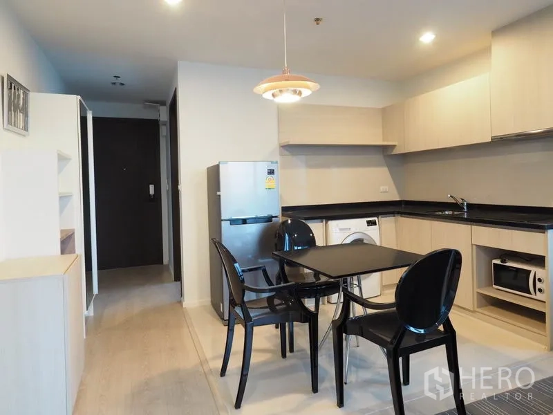 Condominium for rent in Sathon, Bangkok - Dining area beside kitchen with black table and chairs, refrigerator and pendant light.