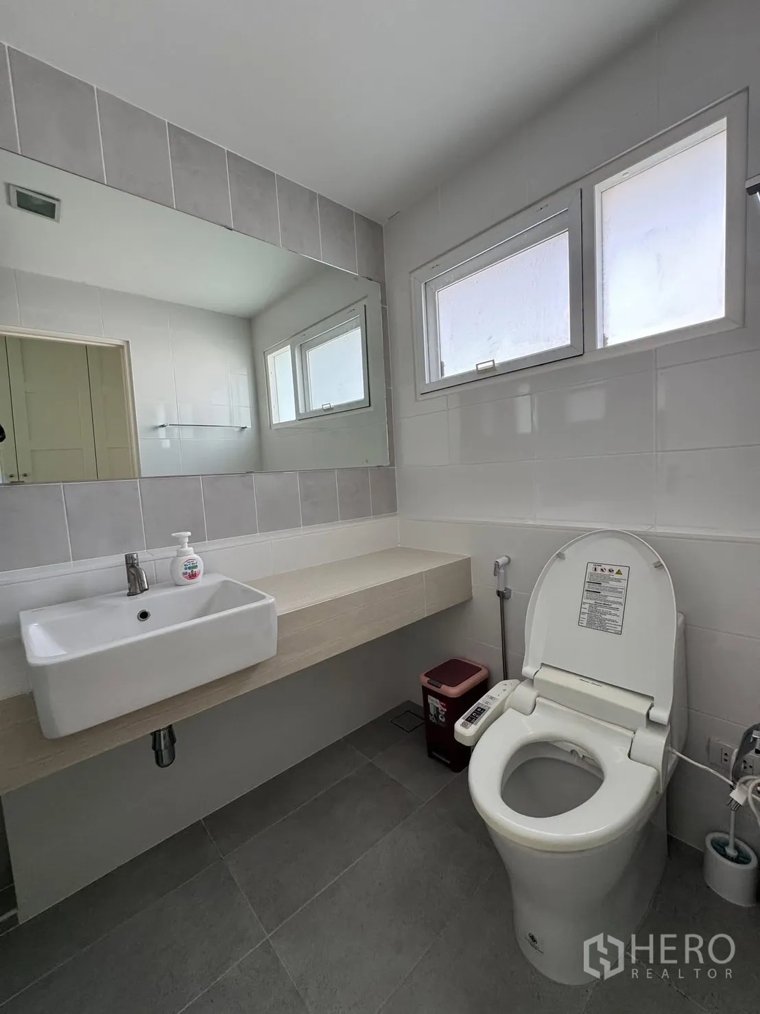 Detached House for rent in Bang Phli, Samut Prakan - Second bathroom with long vanity, sink and bidet toilet under high windows.