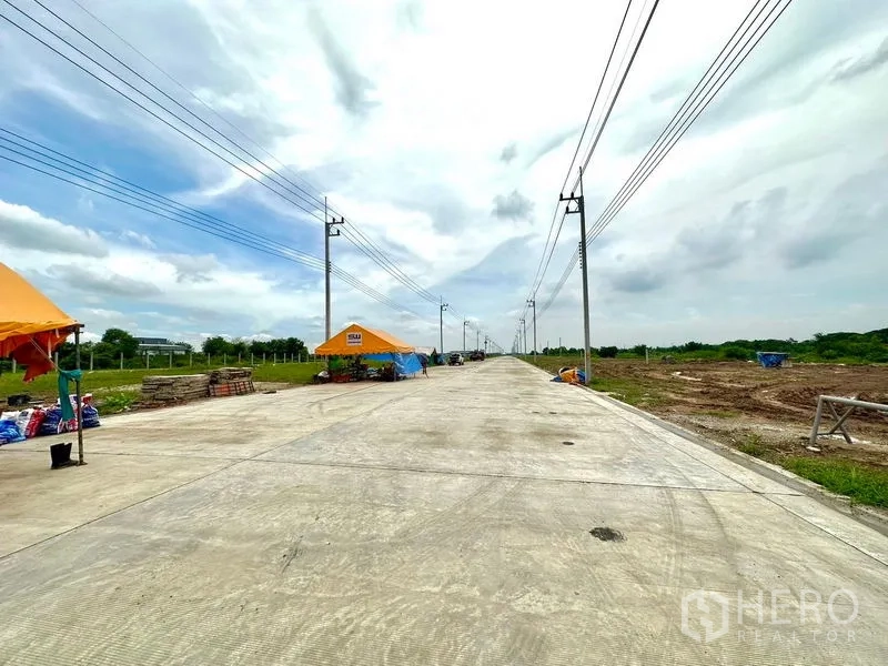 Land for sale in Lam Luk Ka, Pathum Thani - Straight boulevard‑style concrete road with utilities and land plots on both sides inside the estate.