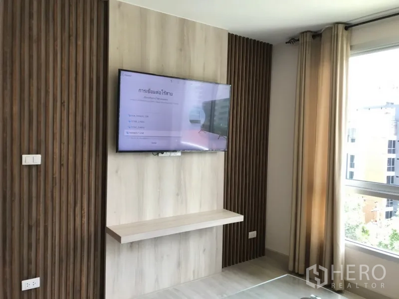 คอนโด ให้เช่าในWatthana, Bangkok - ห้องสว่างพร้อมทีวีติดผนังลายไม้ ข้างหน้าต่างบานใหญ่กับผ้าม่านสีเบจ