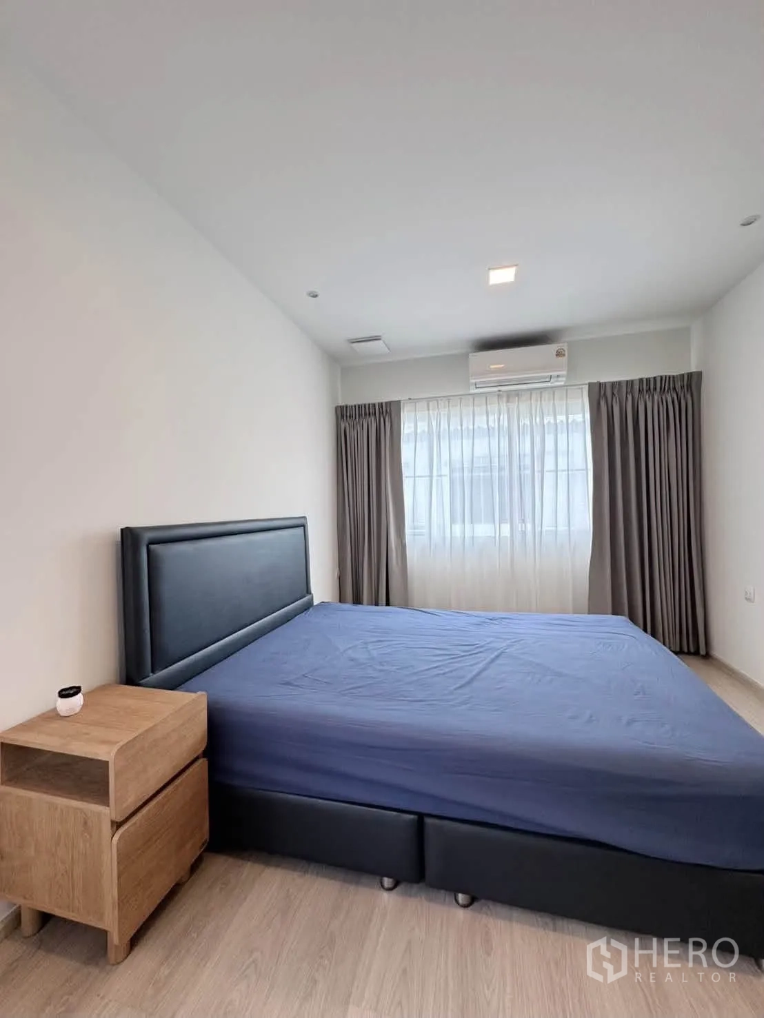 Detached House for rent in Bang Phli, Samut Prakan - Bedroom with dark upholstered bed, bedside table, air conditioner, and draped windows.