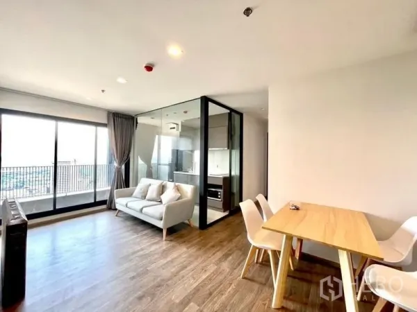 Condominium for rent in Chatuchak, Bangkok - Bright living area with sofa, dining set, glass-walled kitchen and balcony with city view at Life Ladprao Valley.