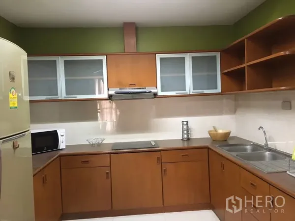 Condominium for rent in Watthana, Bangkok - L-shaped kitchen with wood cabinetry, frosted glass uppers, cooktop, hood, microwave and double sink