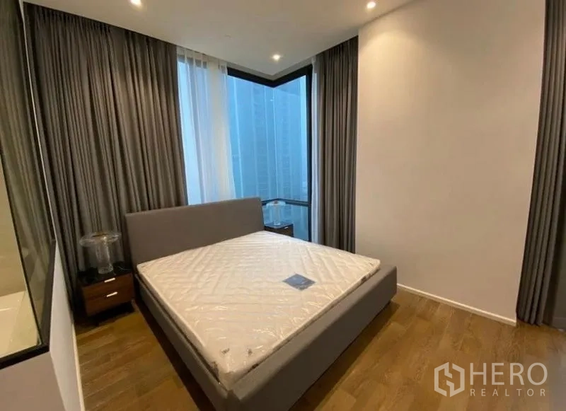 Condominium for rent in Pathum Wan, Bangkok - Primary bedroom with large windows, city outlook, queen bed, bedside tables, and blackout curtains.
