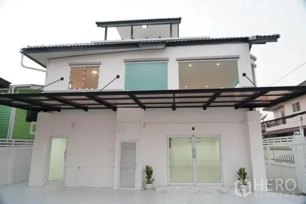 Detached House for sale in Bang Bon, Bangkok - Rear exterior of a two‑storey white detached house with large windows, sliding doors and a covered terrace.
