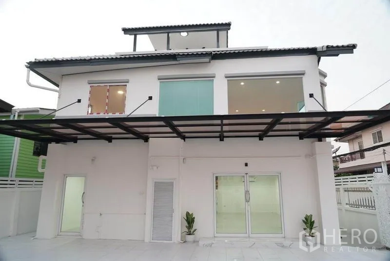 Detached House for sale in Bang Bon, Bangkok - Rear exterior of a two‑storey white detached house with large windows, sliding doors and a covered terrace.