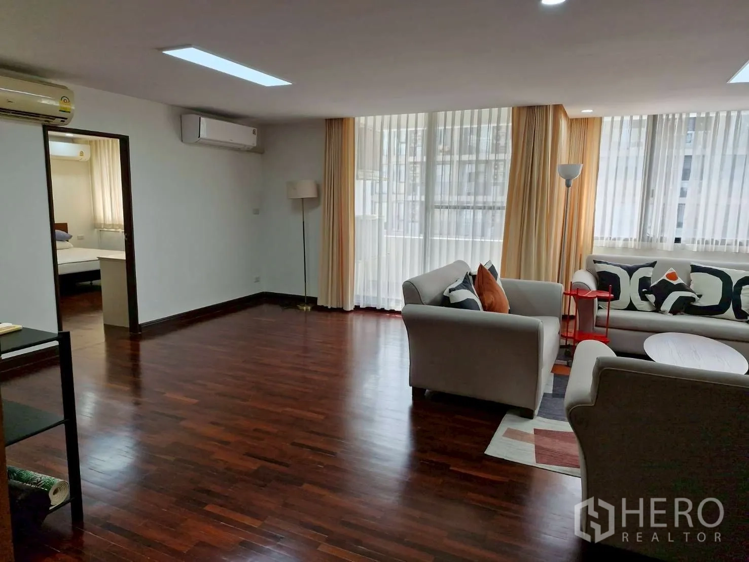 Condominium for rent in Khlong Toei, Bangkok - Spacious living room with multiple sofas and large windows with sheer curtains.
