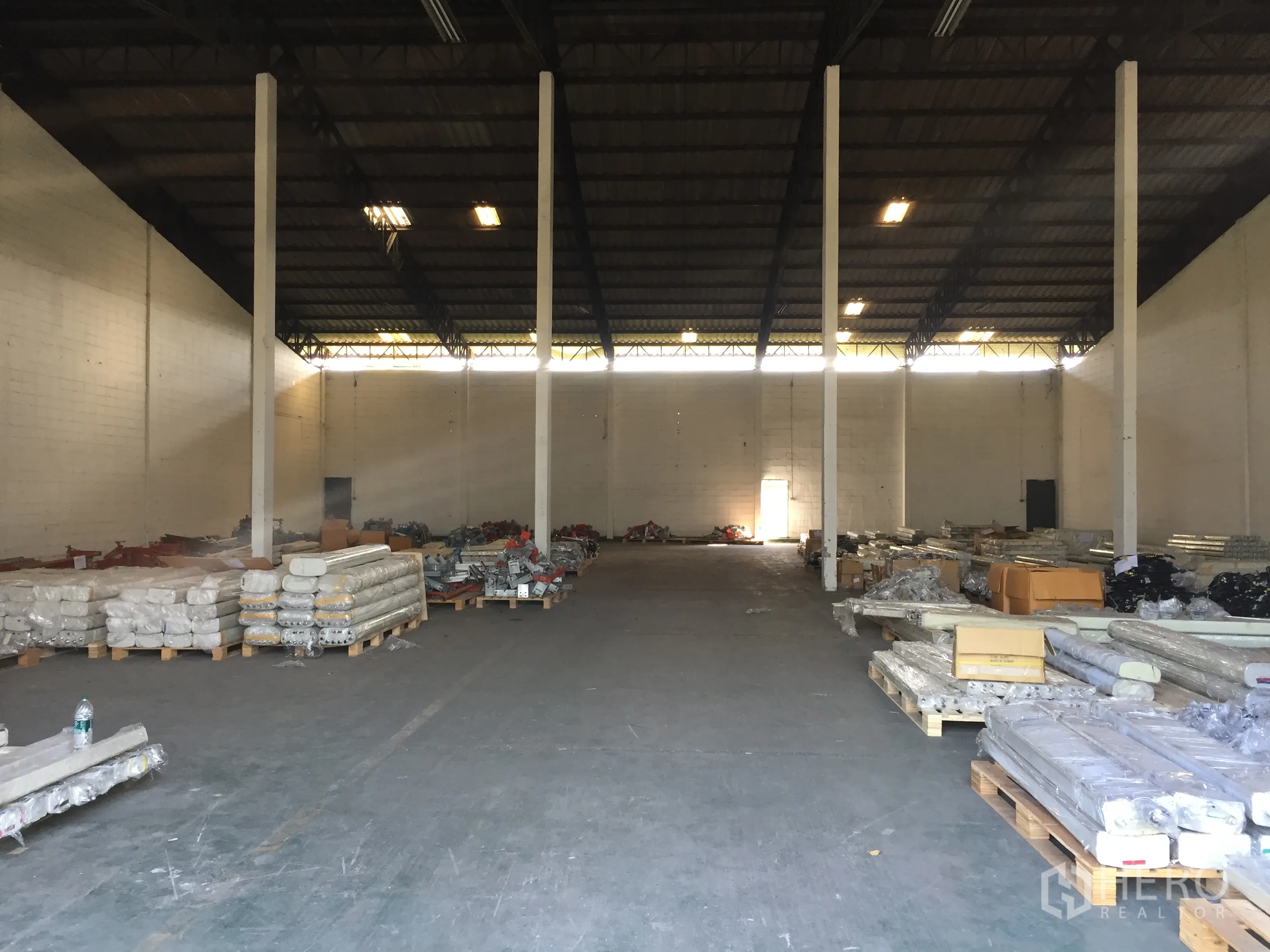 工厂 出租在Pathum Thani - 高挑钢结构屋顶的厂房内部，立柱整齐，地面摆放托盘物料。