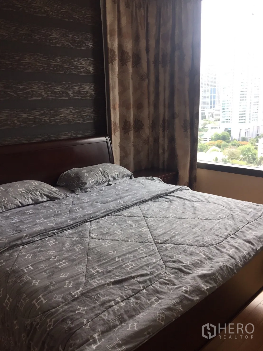 公寓 出租在Khlong Toei, Bangkok - 卧室一角，靠窗可见城市景观与花纹窗帘。