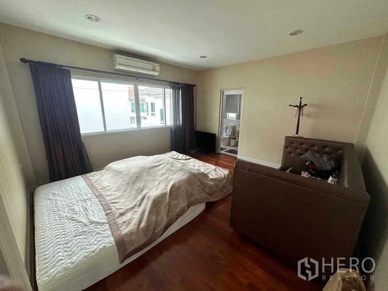 Detached House for sale in Saphan Sung, Bangkok - Spacious bedroom with wide window, air conditioner and access to an ensuite bathroom.