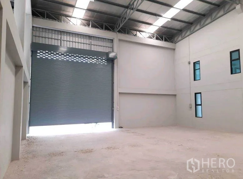 Factory for rent or sale in Bang Bua Thong, Nonthaburi - Warehouse bay featuring tall roller shutter door and durable concrete floor.