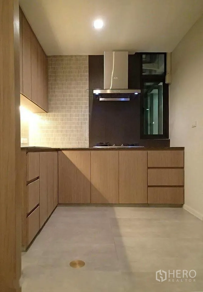Townhouse for rent in Watthana, Bangkok - L-shaped kitchen with wood cabinets, cooktop, and window.