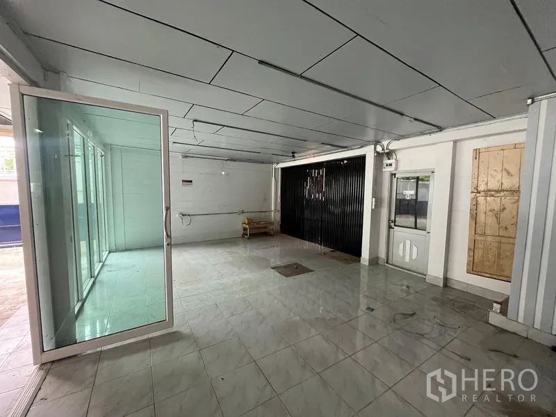 Warehouse for rent in Phra Khanong, Bangkok - Tiled reception area with glass partition and black roll-up shutter inside the warehouse.
