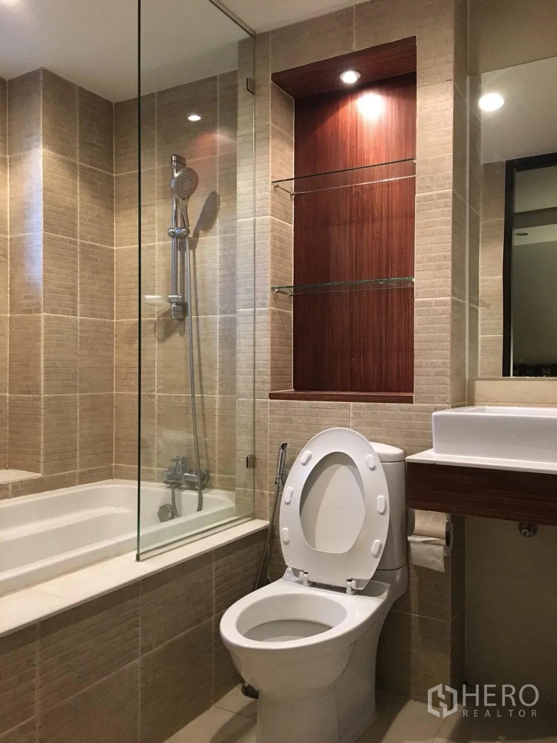 Condominium for rent in Watthana, Bangkok - Beige-tiled bathroom featuring a bathtub with glass screen, handheld shower, toilet, and vanity.