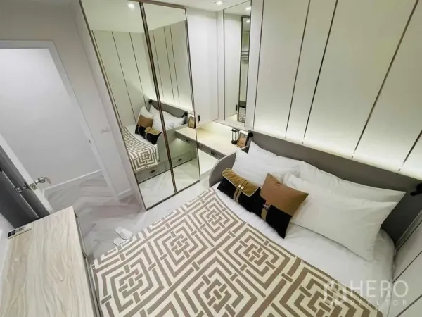Condominium for sale in Yan Nawa, Bangkok - Compact bedroom with mirrored wardrobe, bedside table, and geometric bedspread.
