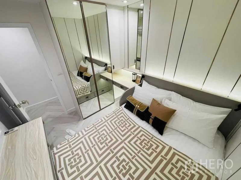 Condominium for sale in Yan Nawa, Bangkok - Compact bedroom with mirrored wardrobe, bedside table, and geometric bedspread.