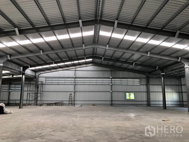 Warehouse for rent in Pak Kret, Nonthaburi - Panoramic interior showing roof trusses, open space and maintenance ladder.